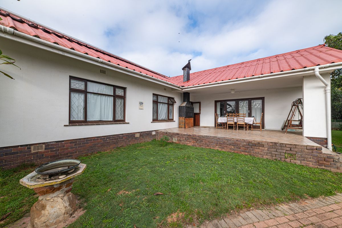 Rear view of the house featuring a covered tiled patio with a built-in braai, overlooking a small garden area with a stone bird bath.