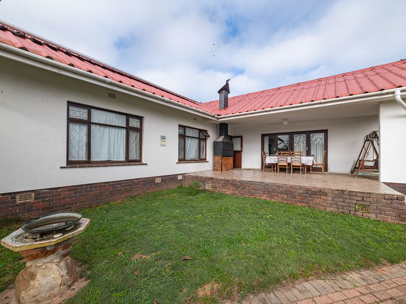 Rear view of the house featuring a covered tiled patio with a built-in braai, overlooking a small garden area with a stone bird bath.