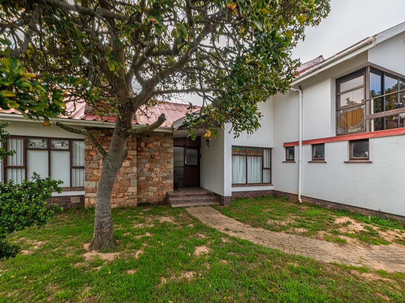 Front elevation of a house featuring stone cladding, a brick pathway, and a balcony, set within a garden area.