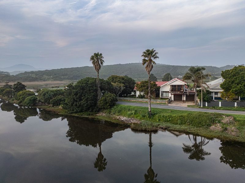Aerial view of a residential property situated along a riverbank, featuring a pitched roof, double garage, and balcony with scenic natural surroundings.