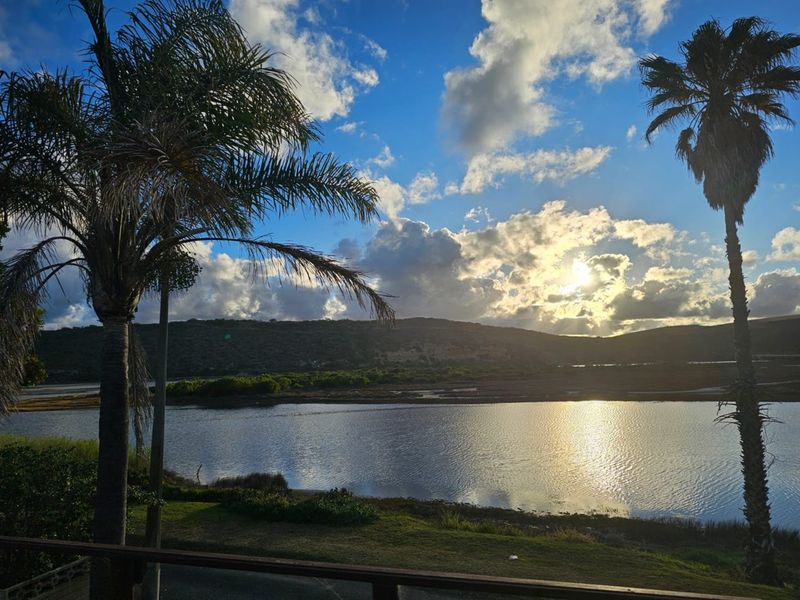 Scenic view of the lagoon and surrounding landscape at sunset, framed by palm trees.