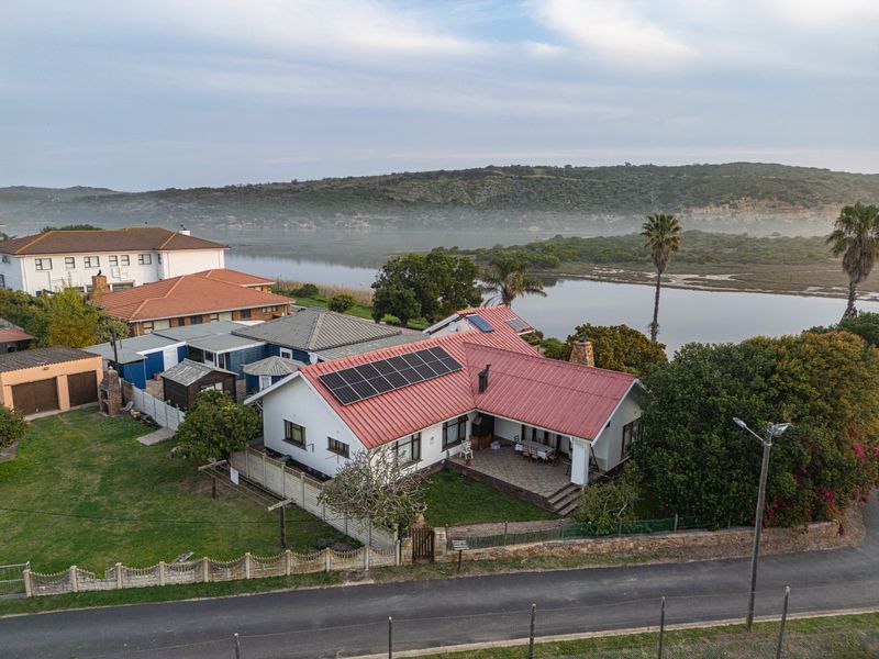 Aerial view of a residential property featuring a metal roof with solar panels, a paved patio, and scenic views of the nearby lagoon.
