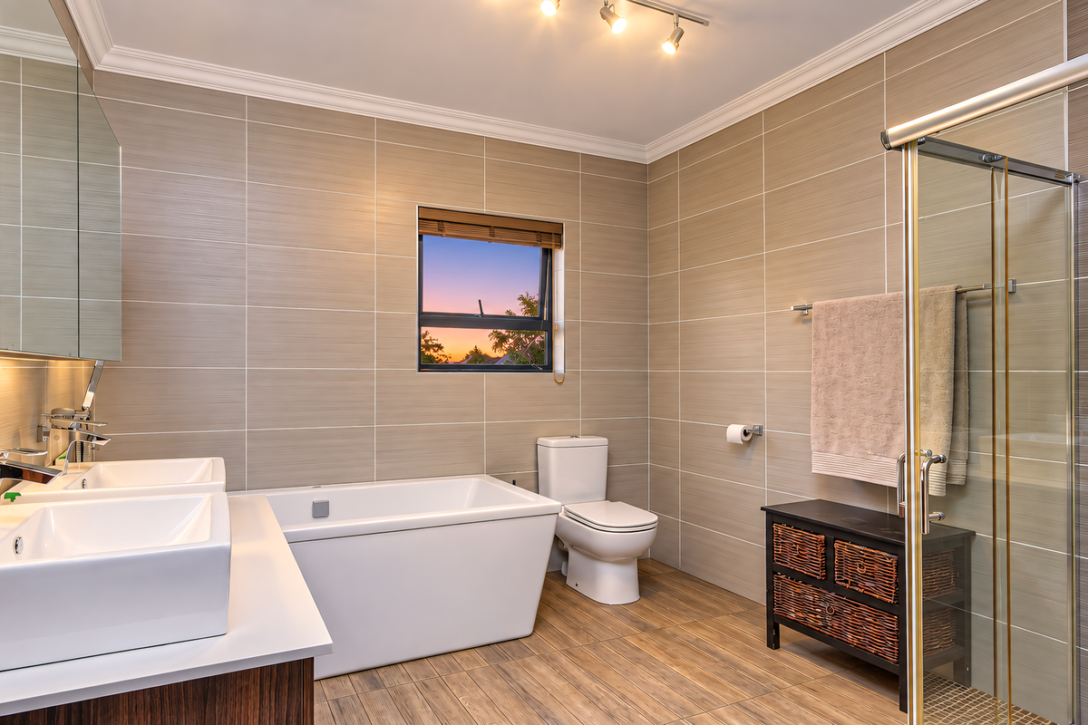 Modern bathroom featuring a double vanity, freestanding bathtub, glass-enclosed shower, and neutral tiled finishes with contemporary lighting.