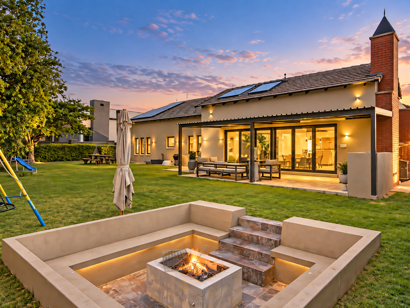A beautifully landscaped rear garden featuring a sunken fire pit, paved patio area, and a covered outdoor entertainment space with modern architectural finishes.