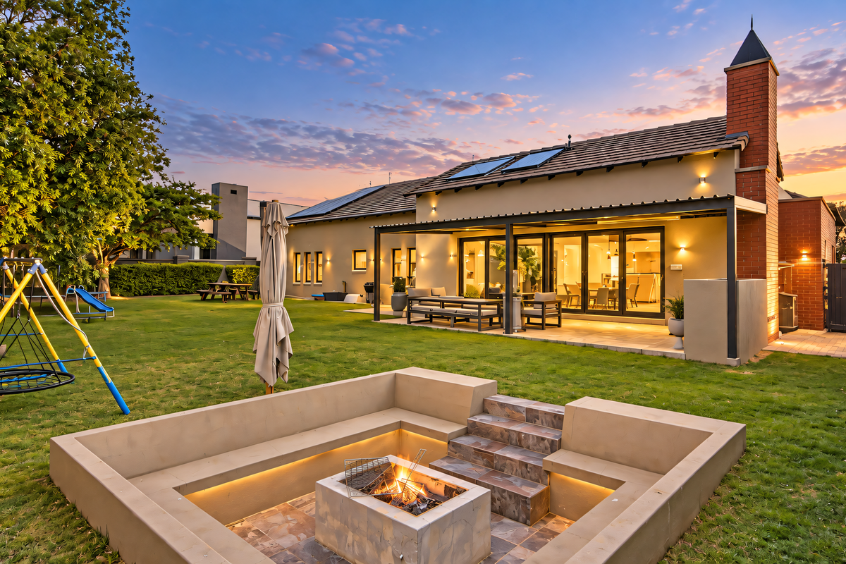 A beautifully landscaped rear garden featuring a sunken fire pit, paved patio area, and a covered outdoor entertainment space with modern architectural finishes.