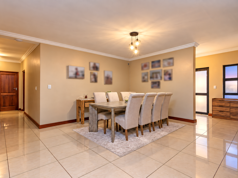 A well-maintained dining room featuring polished tile flooring, crown molding, and a modern pendant light fixture, creating a bright and inviting atmosphere.