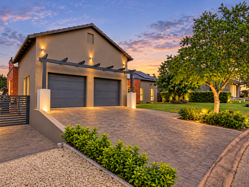 A well-maintained modern home exterior featuring a double garage, paved driveway, and landscaped garden at dusk.