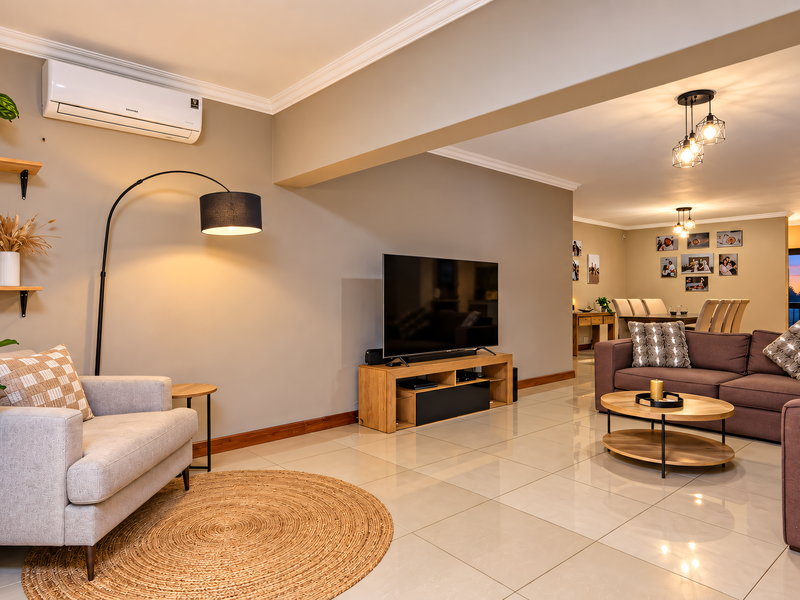 Spacious open-plan living area featuring neutral tones, polished tiled flooring, modern lighting, and a wall-mounted air conditioning unit.
