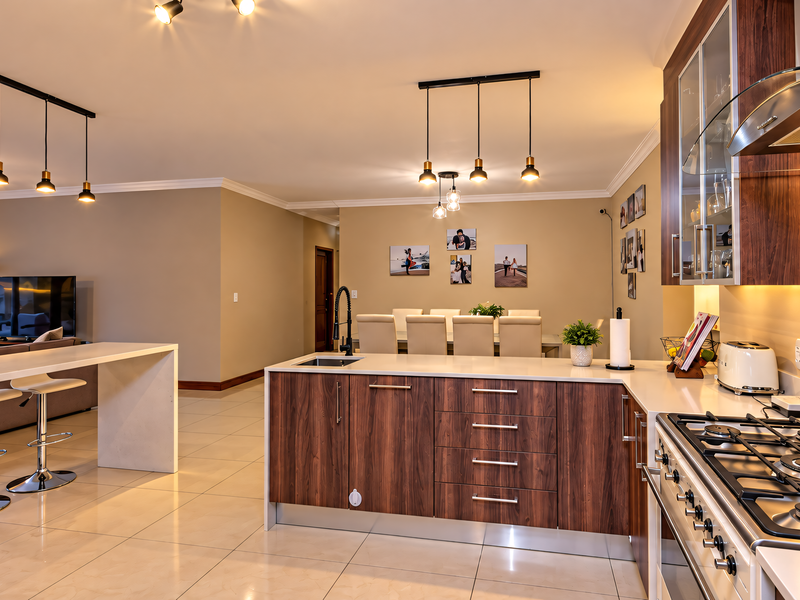 Spacious open-plan kitchen and living area featuring modern wood-finish cabinetry, stone countertops, gas cooktop, and elegant pendant lighting throughout.