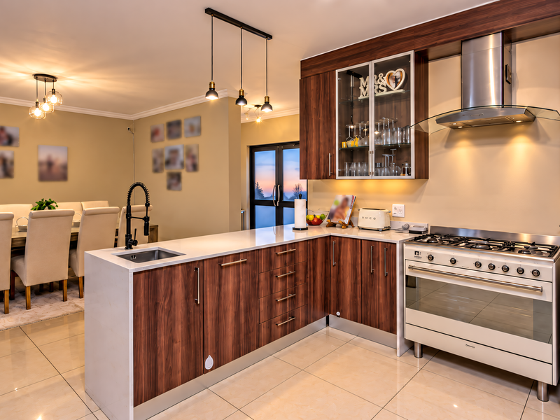 Modern open-plan kitchen and dining area featuring wood-finish cabinetry, stone countertops, a gas stove with extractor, and sleek tiled flooring.
