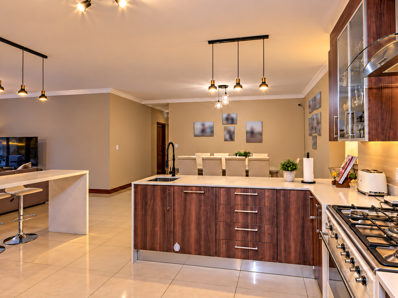 Spacious open-plan kitchen and living area featuring modern wood-finish cabinetry, stone countertops, gas hob, and integrated lighting, creating a seamless flow for entertaining.