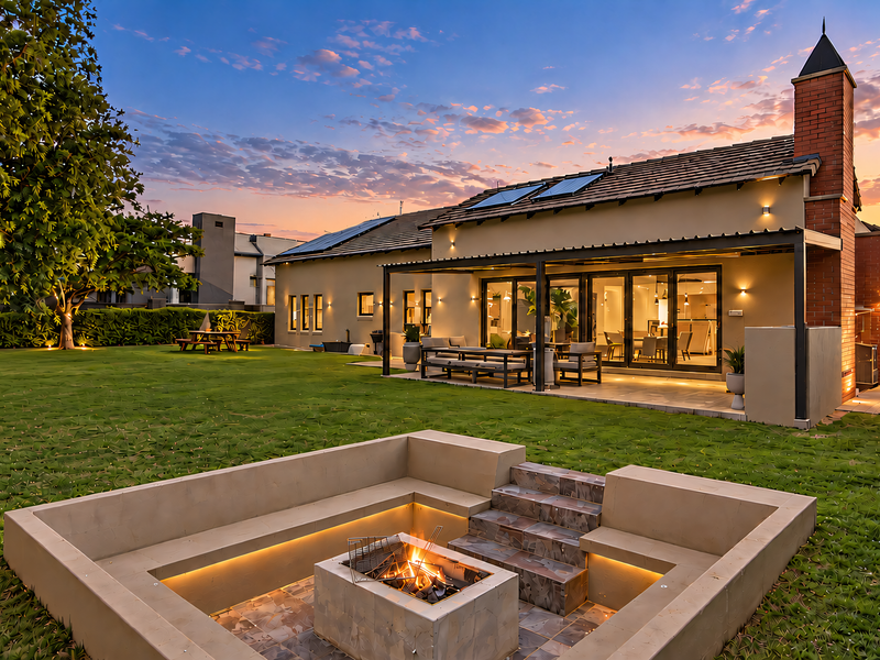 A beautifully landscaped rear garden featuring a sunken fire pit with built-in seating, a covered patio, and a well-maintained home exterior at sunset.
