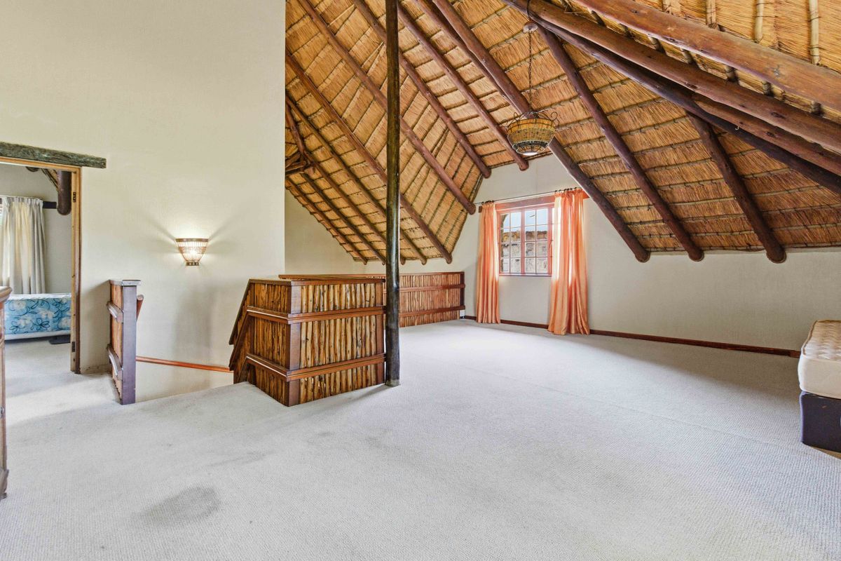 Spacious loft-style bedroom featuring a high vaulted thatched ceiling with exposed timber rafters and a timber balustrade overlooking the lower level.