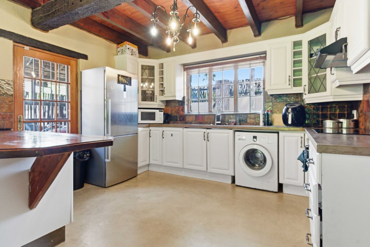 A rustic kitchen featuring exposed timber ceiling beams, white cabinetry, a tiled backsplash, and a breakfast bar, offering a warm and functional cooking space.