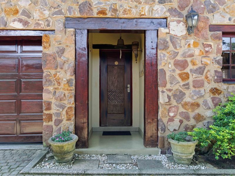 Front entrance of a townhouse featuring a rustic stone facade, timber door frame, and adjacent garage door.