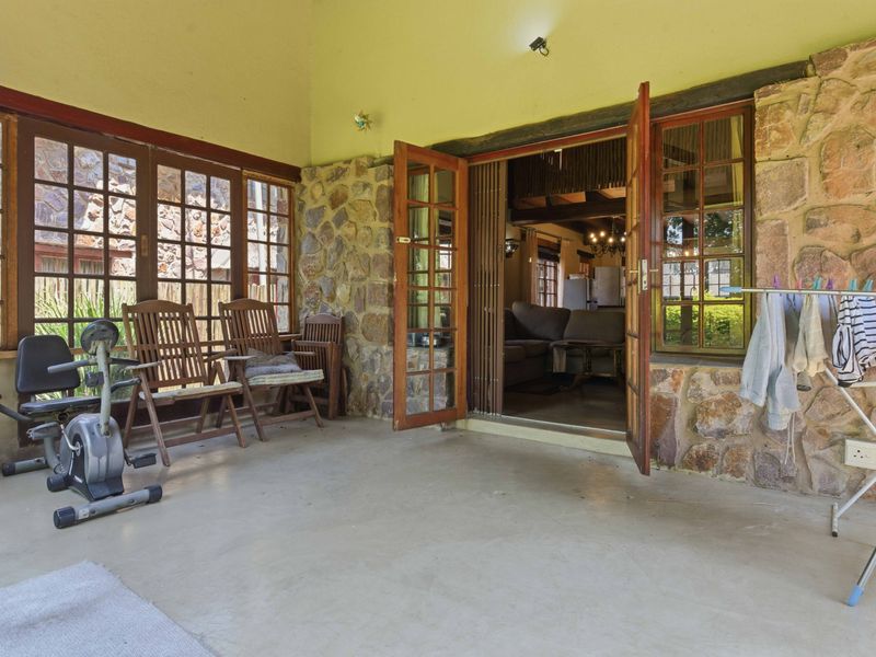 Covered patio area featuring rustic stone wall cladding, timber-framed glass doors, and concrete flooring, providing a seamless transition to the interior living space.