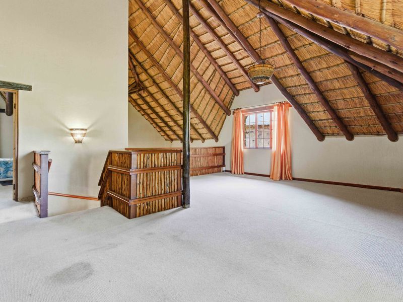 Spacious loft-style bedroom featuring a high vaulted thatched ceiling with exposed timber rafters and a timber balustrade overlooking the lower level.