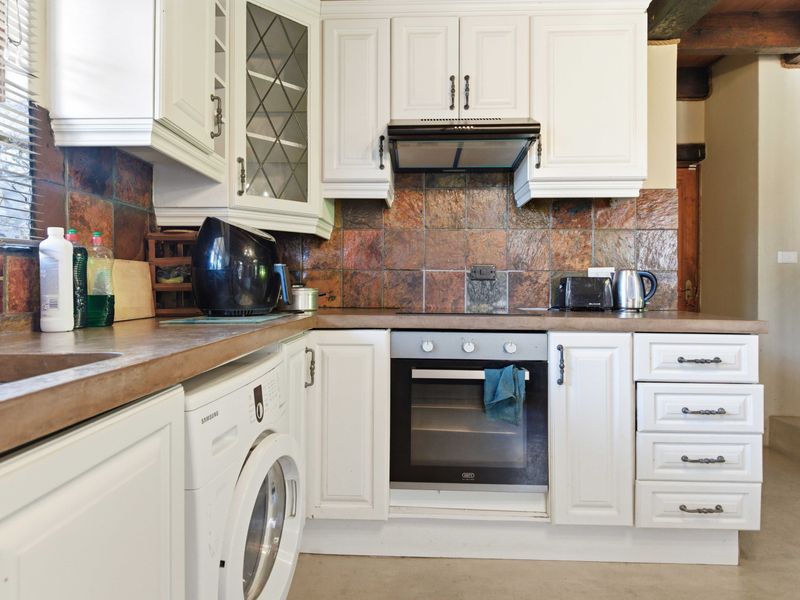 A functional kitchen featuring white cabinetry, stone tile backsplash, integrated oven, and hob, providing a practical workspace with ample storage.