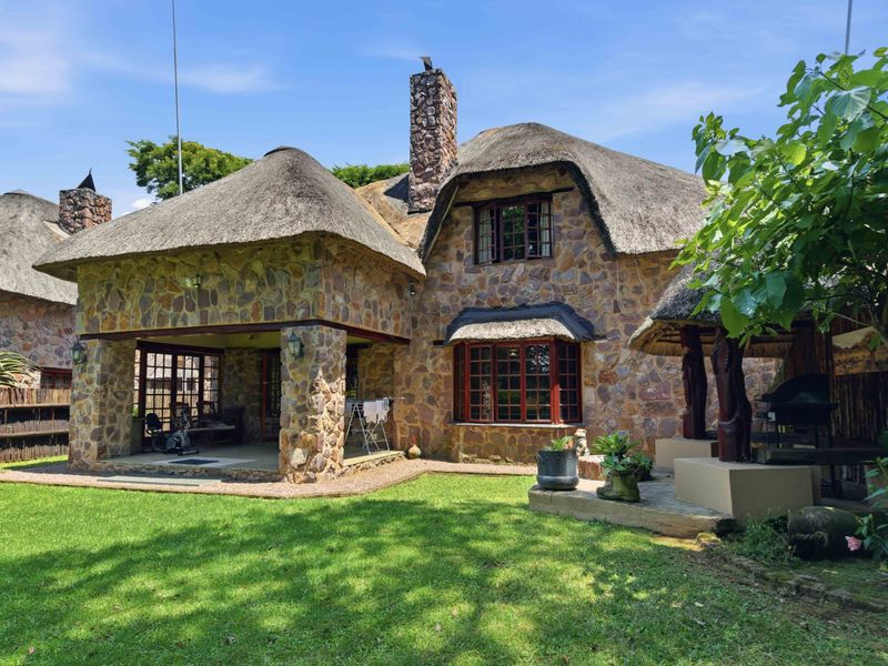 Rear view of a charming townhouse featuring traditional stone cladding, a thatched roof, a covered patio, and a built-in outdoor braai area.