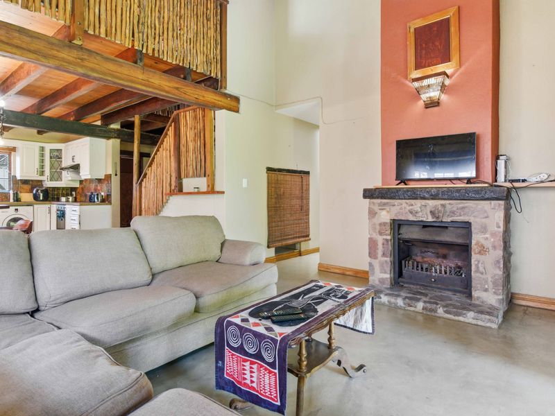 Open-plan living area featuring a stone fireplace, exposed timber beams, and a mezzanine level, seamlessly connected to a functional kitchen space.