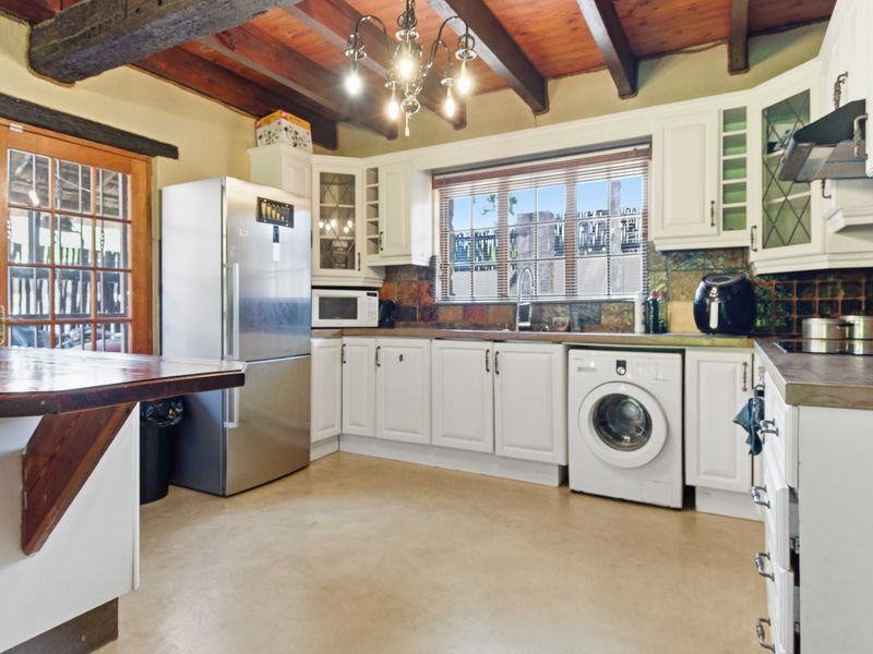 A rustic kitchen featuring exposed timber ceiling beams, white cabinetry, a tiled backsplash, and a breakfast bar, offering a warm and functional cooking space.