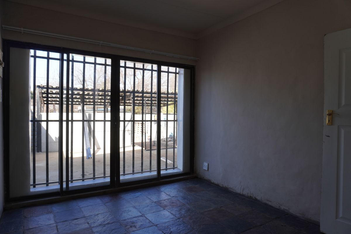 An empty living room featuring dark slate-style floor tiles, a large sliding glass door with security bars, and access to an outdoor area.