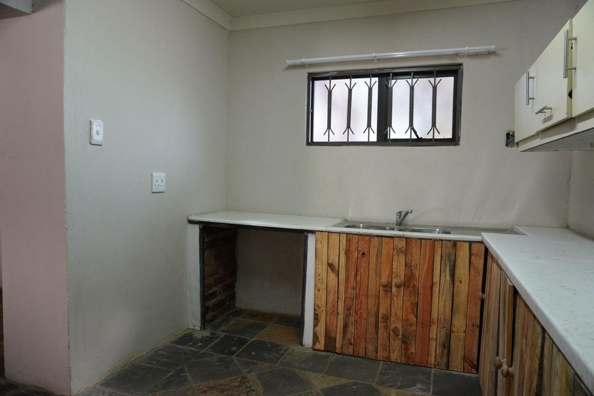 A functional kitchen area featuring a double sink, laminate countertops, and rustic wooden cabinetry with space for under-counter appliances.