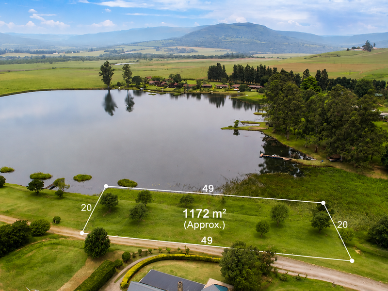 An aerial view of a 1172 square meter vacant residential plot featuring scenic lake frontage and surrounding natural landscape.