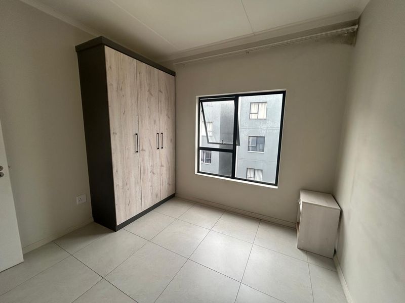 A bright, empty bedroom featuring neutral tiled flooring, a modern built-in wardrobe, and an aluminium-framed window.