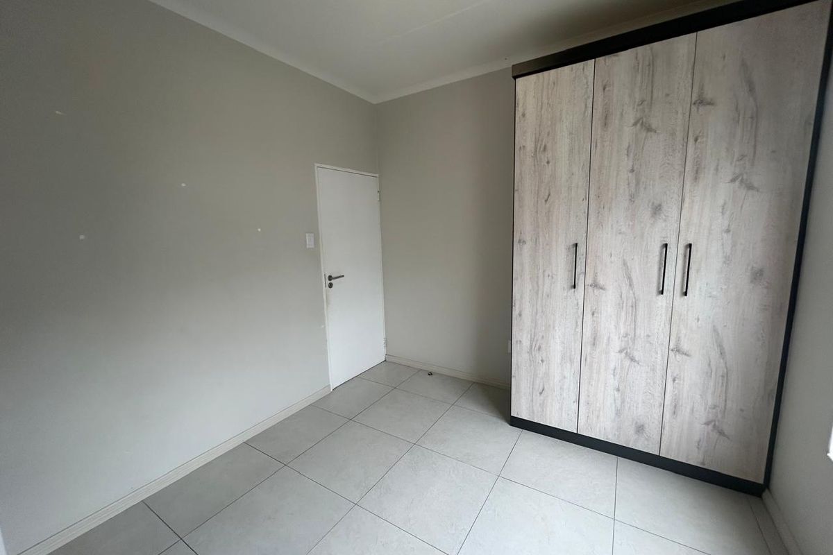 A clean, empty bedroom featuring neutral tiled flooring and a modern built-in wardrobe with wood-grain finish doors.