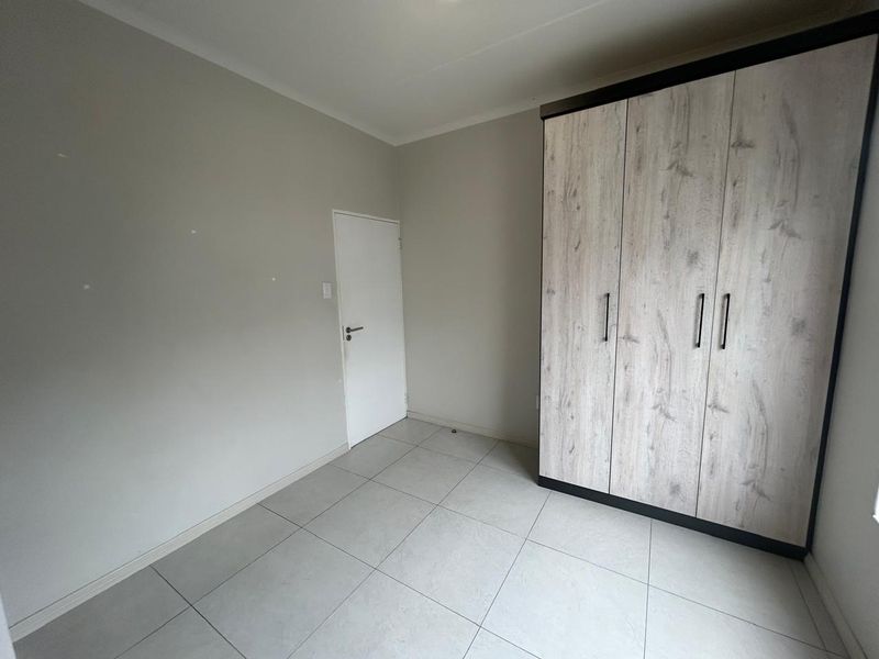 A clean, empty bedroom featuring neutral tiled flooring and a modern built-in wardrobe with wood-grain finish doors.