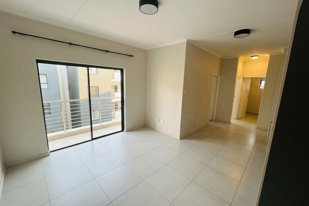 Bright and spacious open-plan living area featuring neutral tiled flooring, modern ceiling lighting, and a sliding glass door leading to a private balcony.