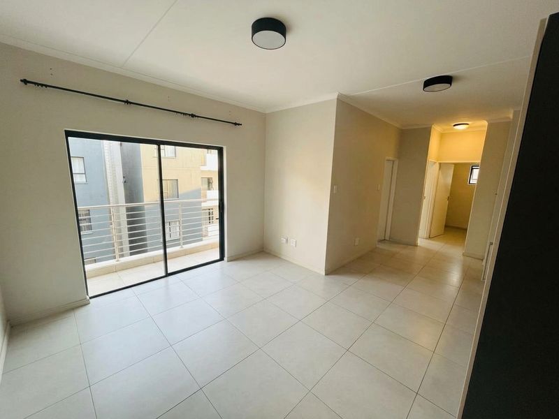 Bright and spacious open-plan living area featuring neutral tiled flooring, modern ceiling lighting, and a sliding glass door leading to a private balcony.