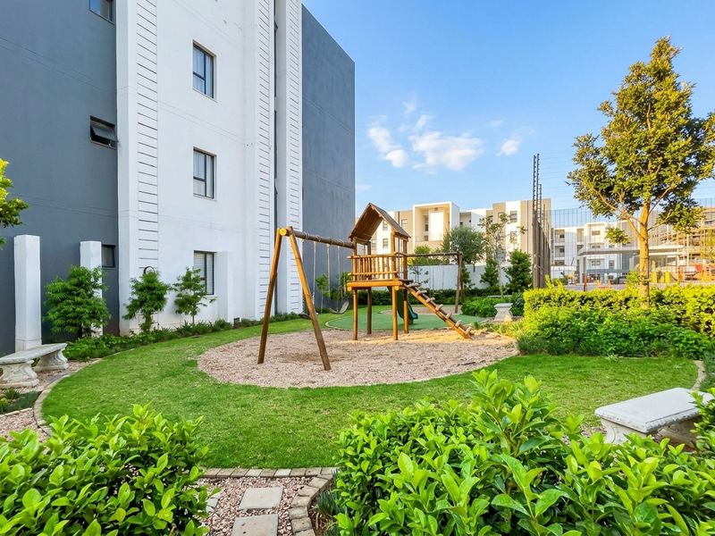 Well-maintained communal garden area featuring a wooden playground structure, manicured lawn, stone benches, and secure perimeter fencing.