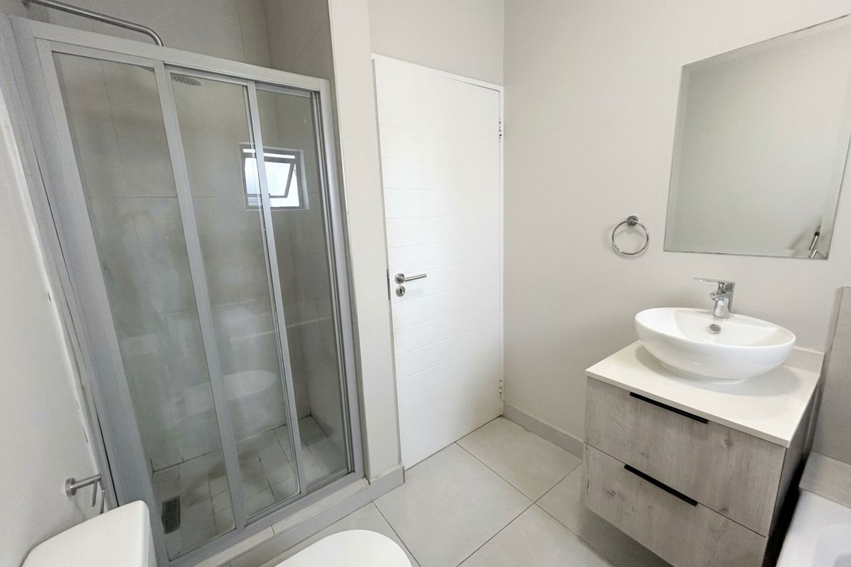 Modern bathroom featuring a glass shower enclosure, a contemporary vanity with a vessel sink, and neutral floor tiling.