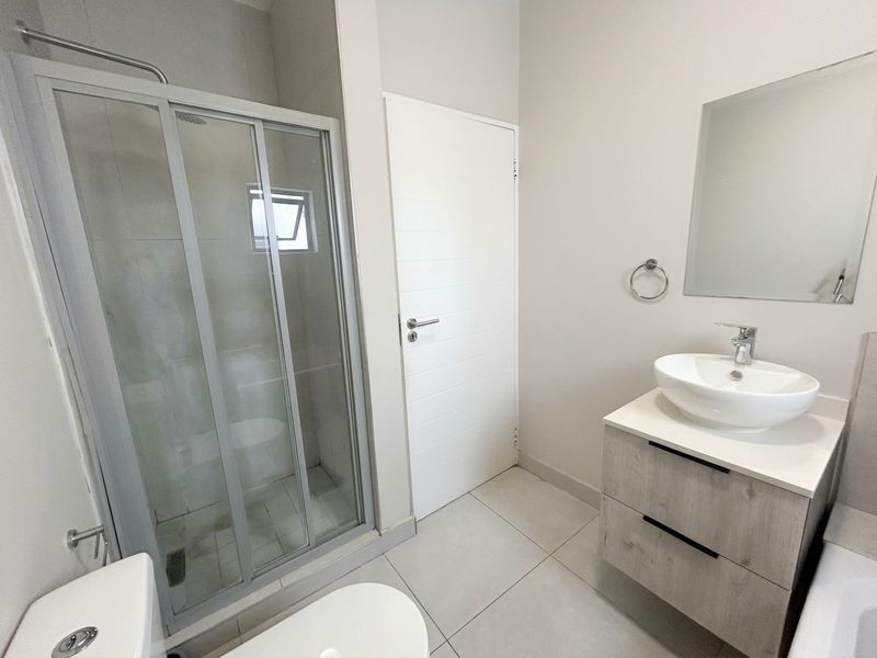 Modern bathroom featuring a glass shower enclosure, a contemporary vanity with a vessel sink, and neutral floor tiling.