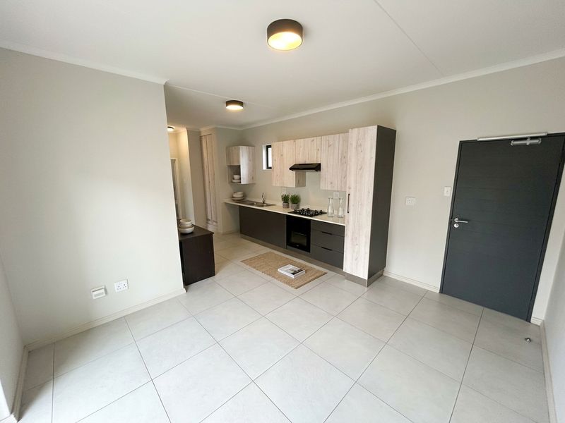 Modern open-plan kitchen featuring light wood and dark grey cabinetry, integrated appliances, and neutral tiled flooring in a clean, well-maintained apartment space.