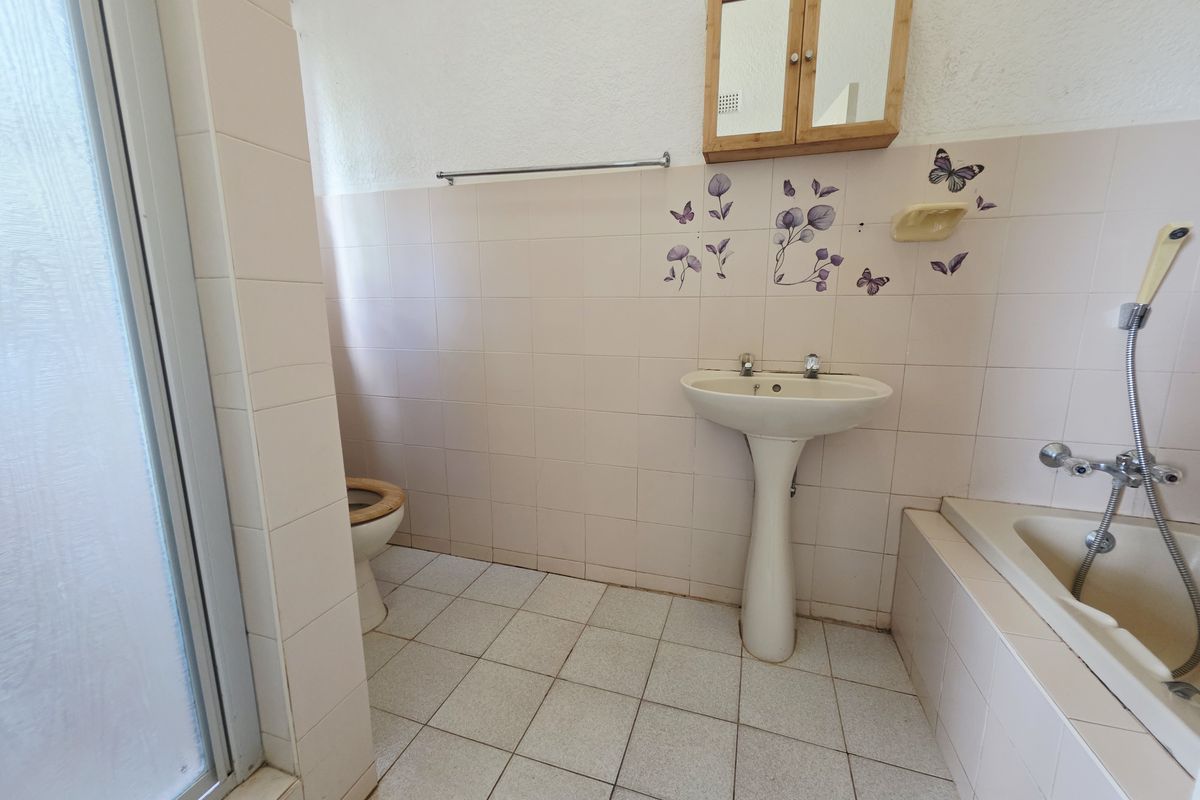 A dated bathroom featuring a pedestal basin, bathtub, shower enclosure, and toilet with original wall tiling and floor finishes.