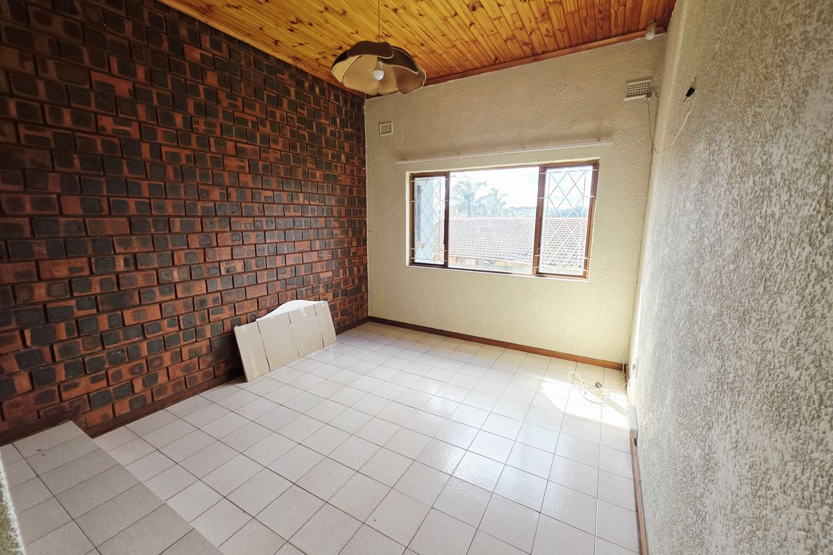 An empty bedroom featuring an exposed brick wall, timber ceiling, and tiled flooring, offering a blank canvas for renovation.
