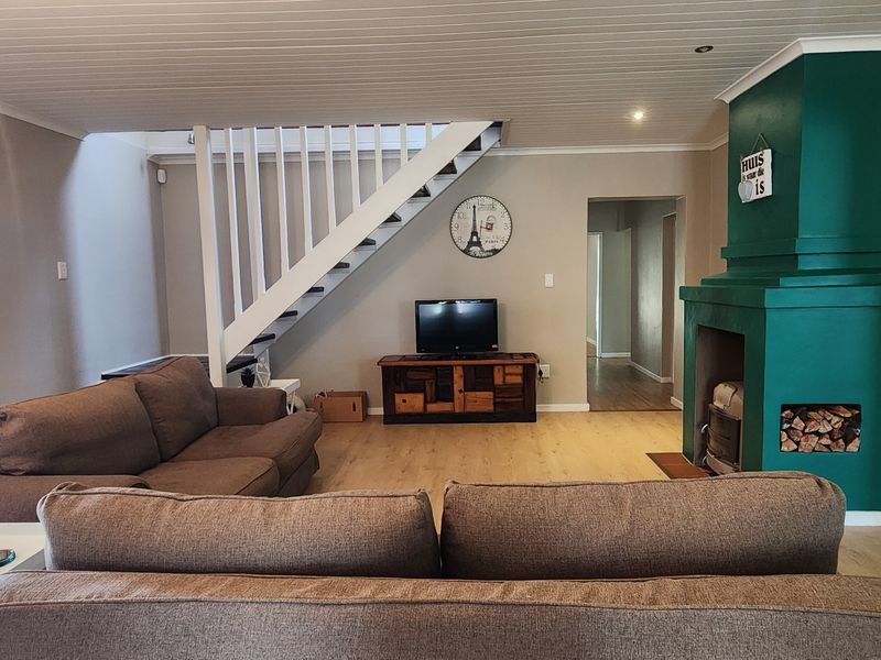 Spacious living room featuring a prominent green fireplace, wooden laminate flooring, and a staircase leading to the upper level.