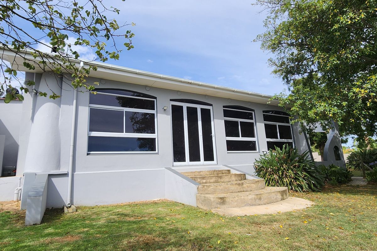 Rear exterior view of the property featuring a painted facade, concrete entrance steps, and large aluminium-framed windows set within a garden area.