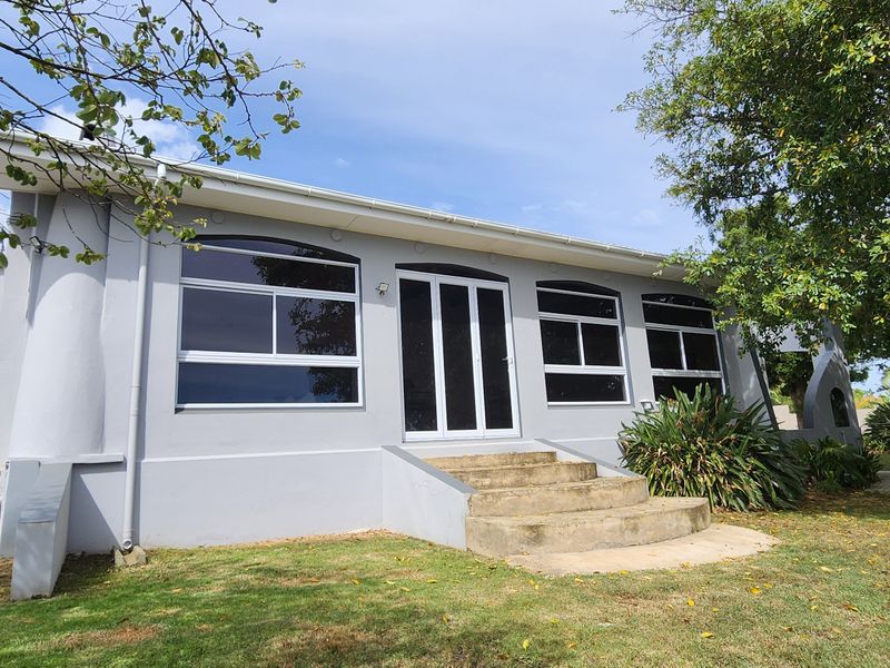 Rear exterior view of the property featuring a painted facade, concrete entrance steps, and large aluminium-framed windows set within a garden area.