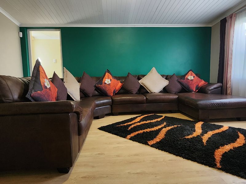 A spacious living room featuring light-toned laminate flooring, a white tongue and groove ceiling, and a bold green accent wall.
