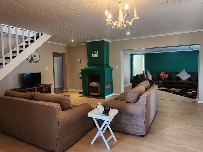 Spacious open-plan living area featuring a central fireplace, staircase, laminate flooring, and a distinctive tongue and groove ceiling.