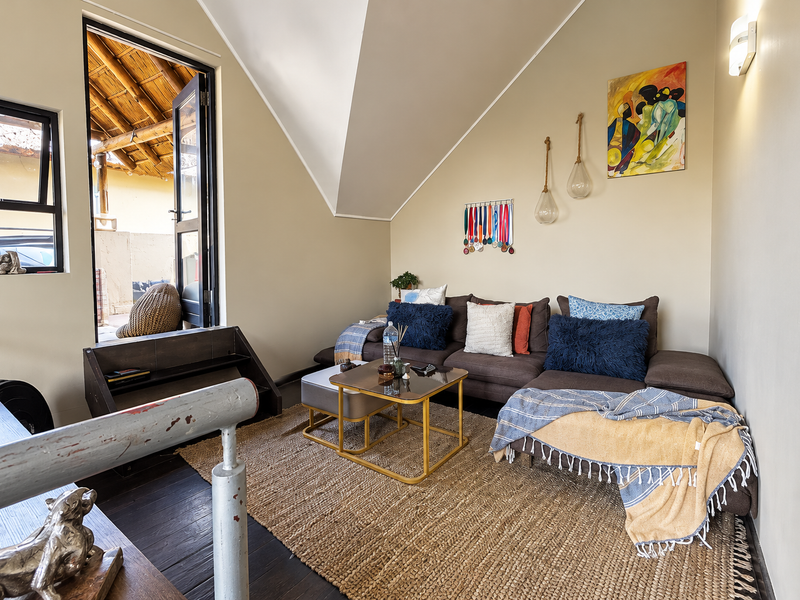 A cozy living room featuring a vaulted ceiling, dark timber flooring, and direct access to an outdoor patio area through an aluminium door.