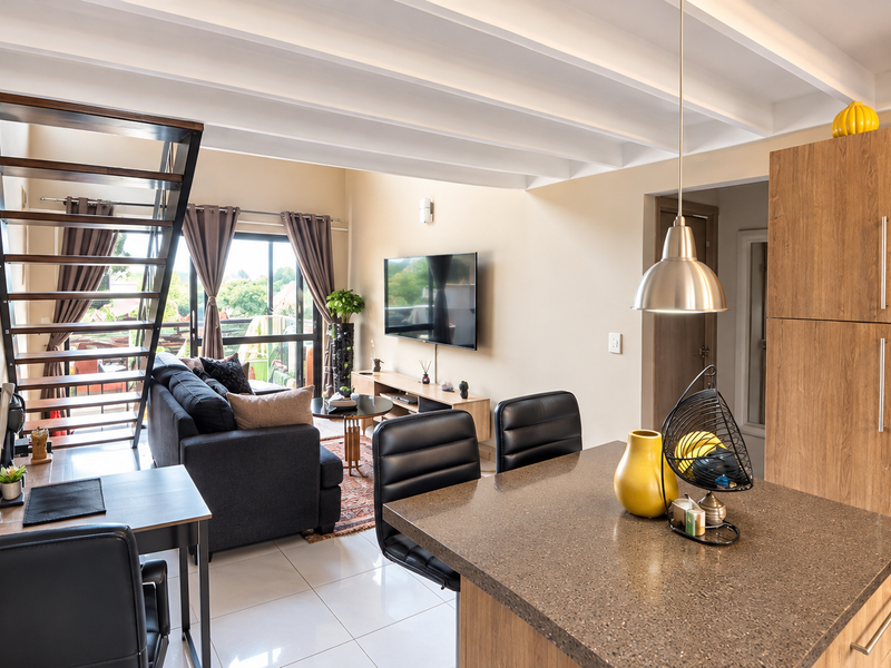Modern open-plan living area featuring a kitchen with stone countertops, exposed beam ceilings, and a staircase leading to an upper level.
