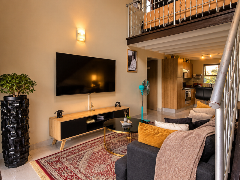 Open-plan living area featuring a mezzanine level with a metal staircase, integrated kitchen cabinetry, and modern tiled flooring in a well-maintained apartment setting.