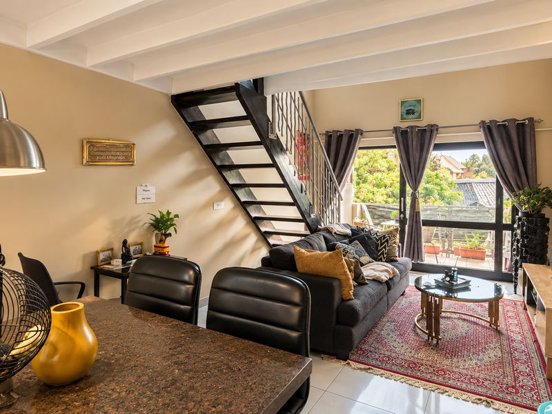 Open plan living and dining area featuring exposed ceiling beams, a staircase, and large sliding glass doors leading to an outdoor balcony.
