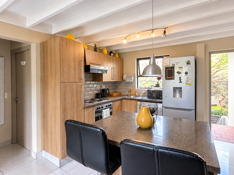 A functional kitchen featuring wood-finish cabinetry, stone countertops, a tiled backsplash, and an exposed beam ceiling, with direct access to an outdoor area.