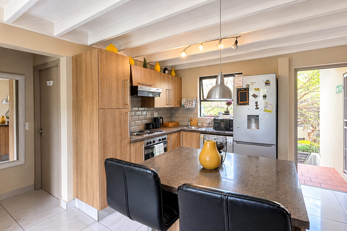 A functional kitchen featuring wood-finish cabinetry, stone countertops, a tiled backsplash, and an exposed beam ceiling, with direct access to an outdoor area.